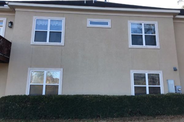 After: a freshly soft washed beige stucco two story home four double windows and one small horizontal window in the center, with neatly trimmed green hedges in front.